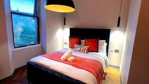 A bedroom with a large bed, a window, and a hanging light fixture.