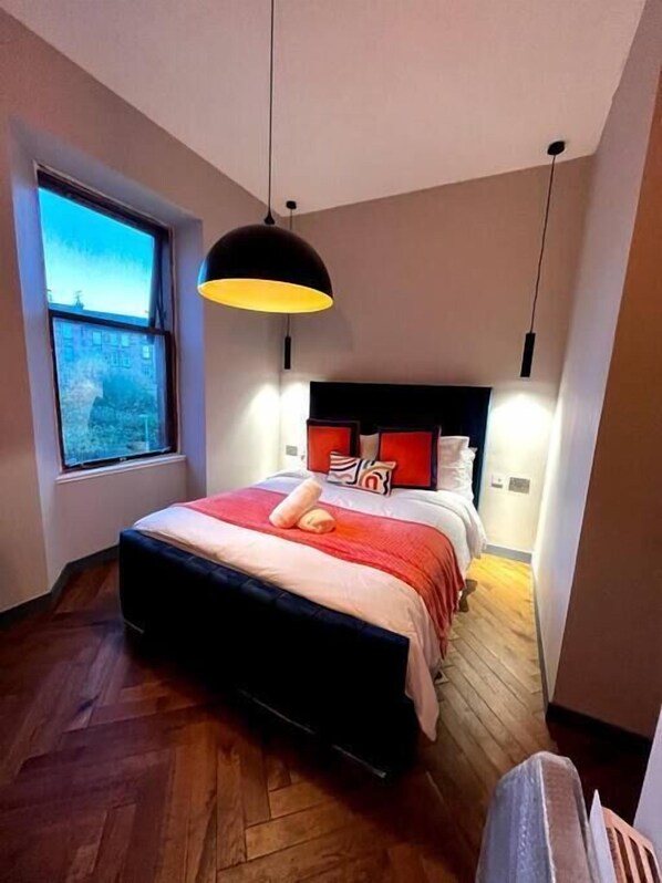 A bedroom with a large bed, a window, and a hanging light fixture.