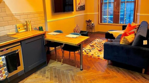 A compact living space with a kitchenette, a sofa, a dining table, and a large window.