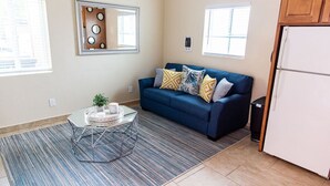 A living room with a blue sofa, patterned cushions, a glass coffee table, and a striped rug. - The PB Spot 1BR w/ Parking (San Diego)