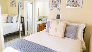 A bedroom with a bed, a mirror, a door, and a bathroom visible through an open door. - The PB Spot 1BR w/ Parking (San Diego)