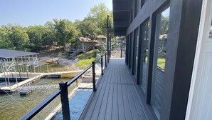 Een houten terras met een hekwerk, met uitzicht op een wateroppervlak, een steiger en een gebouw met grote ramen.
