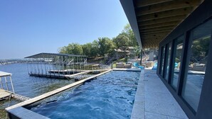 Een zwembad zonder rand met uitzicht op het water en de steiger, een overdekt zitgedeelte en een balkon met glazen wanden.
