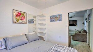 Quarto com cama, parede branca com duas pinturas e estante embutida.