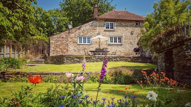 A stone house with a well-maintained garden, a patio with outdoor furniture, and a stone wall.