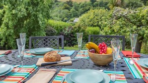 An outdoor dining table set with plates, cutlery, glasses, a loaf of bread, and a bowl of fruit.