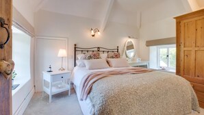 A bedroom with a bed, bedside table, lamp, mirror, and wardrobe.