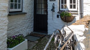A white stone building with a black door, a sign reading "Court Cottage," and flower boxes on the windowsills.