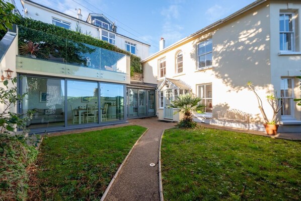 Ein modernes Haus mit Wintergarten, kleinem Garten und einem Weg.