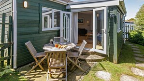 Ein gemütlicher Essbereich im Freien mit Tisch und Stühlen, ein kleiner Garten und ein Gebäude mit einer Schiebeglastür.