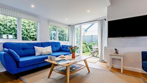 Ein Wohnzimmer mit einem blauen Sofa, einem Couchtisch und einem an der Wand befestigten Fernseher.