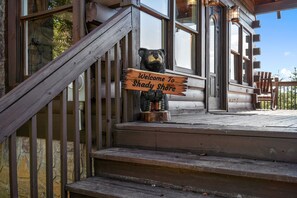 A wooden staircase leading to a porch with a bear statue holding a sign that reads "Welcome to Shady Shore."