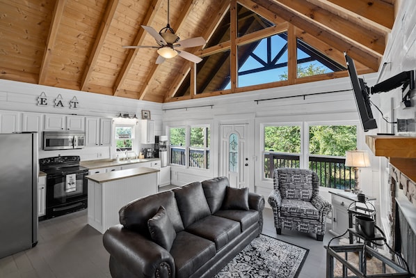 A spacious kitchen with white cabinetry, a black leather sofa, and a dining area with a patterned chair.
