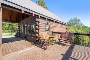 A log cabin with a wooden deck, rocking chairs, and a covered porch.