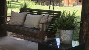 Eine Holzschaukel mit Kissen, ein Blumentopf und ein gemustertes Teppich auf einer Terrasse.