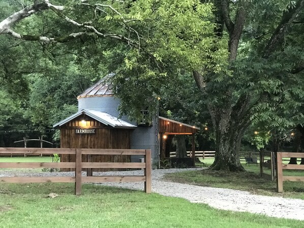 Una casa de campo rústica con fachada de madera y techo de metal, rodeada de abundante vegetación y árboles.