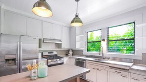Et moderne køkken med rustfrie hårde hvide skabe og et stort vindue med udsigt til grønne områder.