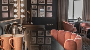 Ett rum med en kaffebryggare, två muggar, en soffa och en vägg med inramade tavlor.