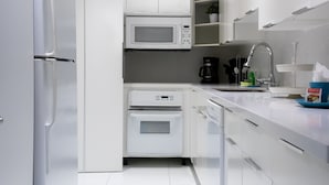 Eine moderne Küche mit weißen Schränken, einem Kühlschrank, einer Mikrowelle, einem Backofen und einer Kaffeemaschine.