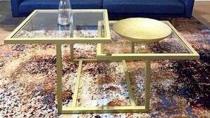 Un canapé bleu avec des coussins marron et rouges, une table basse en verre sur laquelle repose un bol blanc, et un vase décoré de branches.