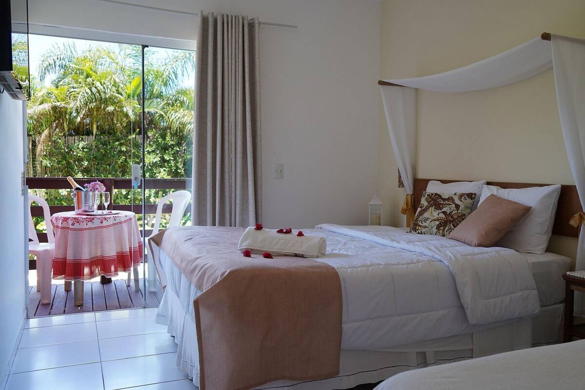 A bedroom with a bed, a nightstand, a bedside table, a window with curtains, and a balcony with a table and chairs.