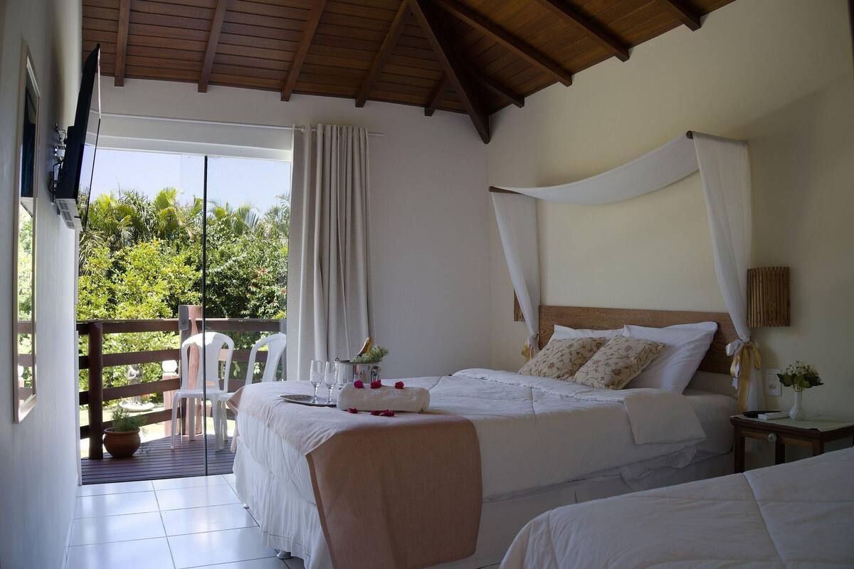 A bedroom with a bed, a bedside table, a nightstand, a window with curtains, a balcony with chairs, and a television.