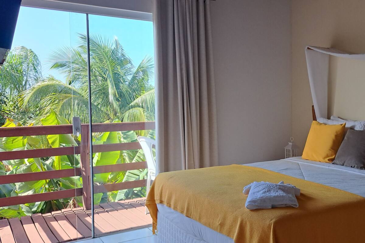 A hotel room with a bed, a nightstand, and a view of palm trees through a balcony.