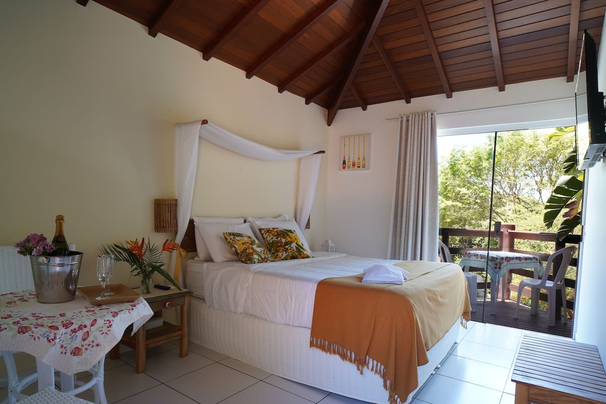 A bedroom with a bed, a nightstand, a table with a floral tablecloth, and a balcony with a table and chairs.