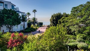 A pathway leading to a beach with lush greenery and a modern building on the left.