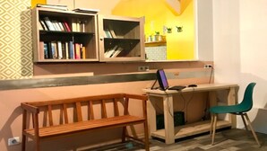 A study area with a wooden desk, a computer, and a chair. There is a bookshelf with books and a mirror above the desk.
