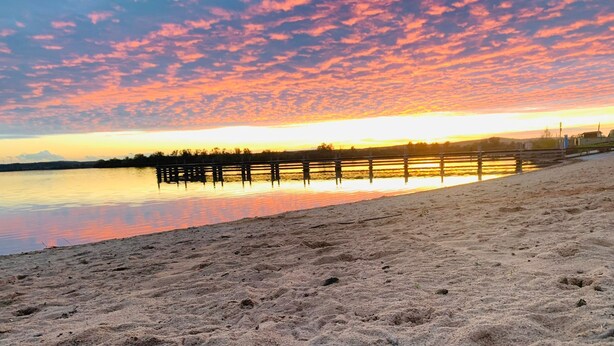 Una playa con un muelle de madera que se adentra en aguas tranquilas durante el atardecer.