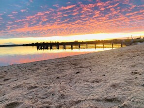 Ein Strand mit einer hölzernen Pier, die sich in ruhiges Wasser bis zum Sonnenuntergang erstreckt.