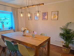 A dining area with a wooden table, chairs, hanging lights, and wall art. - Fully equipped vacation home with large garden-just 7 minutes from the lake (Muhr am See)