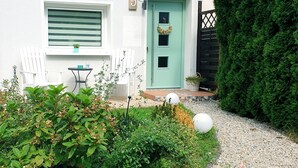 Una casa blanca con puerta verde, sillas blancas y un jardín con senderos de grava.