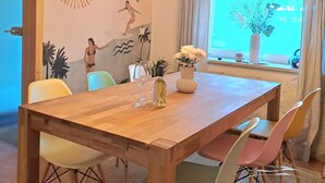 Un comedor con mesa de madera, sillas coloridas, lámparas colgantes y un mural en la pared.