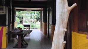 A room with a large wooden tree trunk centerpiece, a tiled floor, and a view of greenery outside. - Koh Chang Garden Lodge Guest  Room G (Klong Son)