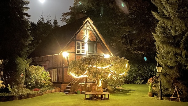 Una casa de madera con techo de paja, rodeada por un jardín cuidado y árboles.