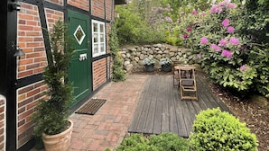 Una casa tradicional con entramado de madera, puerta verde, terraza de madera y pared de piedra.