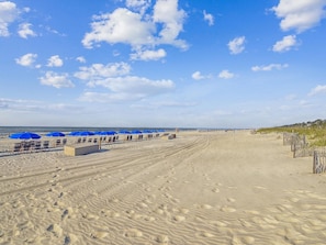 A beach with blue umbrellas and sun loungers, a sandy path, and footprints.