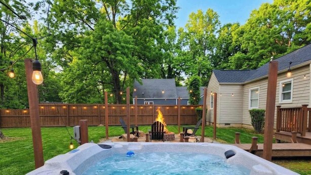 Un patio trasero con un jacuzzi, terraza de madera y un pozo de fuego.