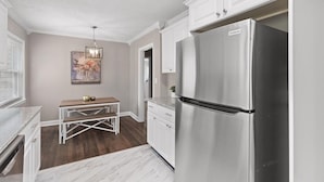 Una cocina moderna con armarios blancos, un refrigerador de acero inoxidable y una mesa de comedor de madera.