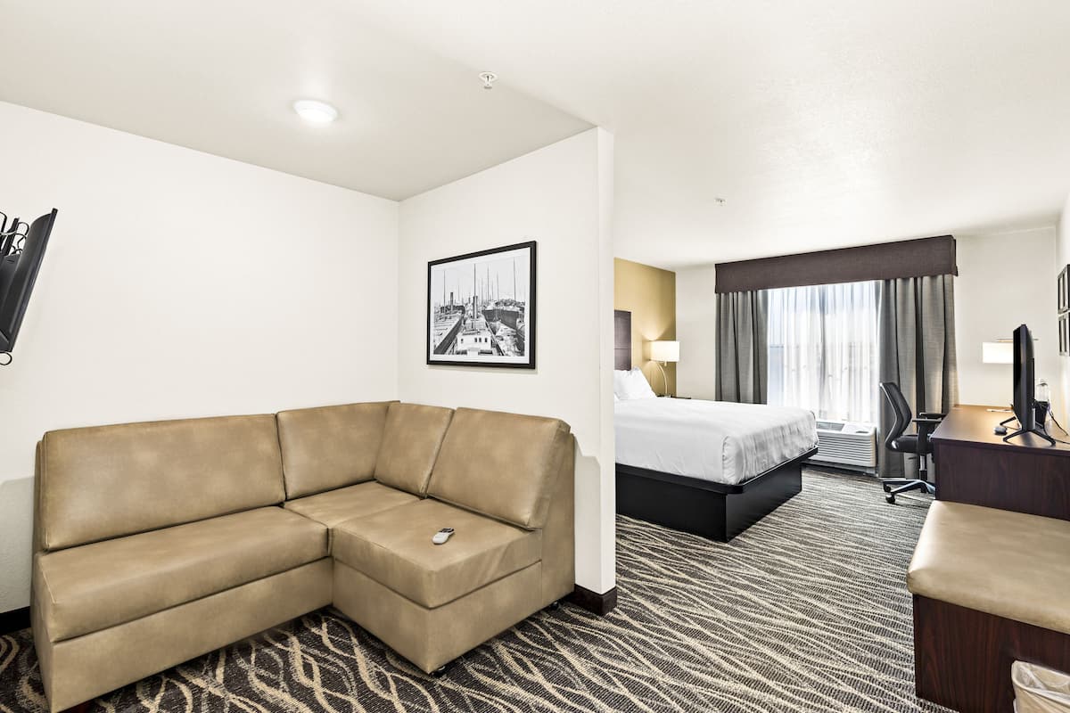 A hotel room with a sofa, a bed, a desk, and a framed picture on the wall.