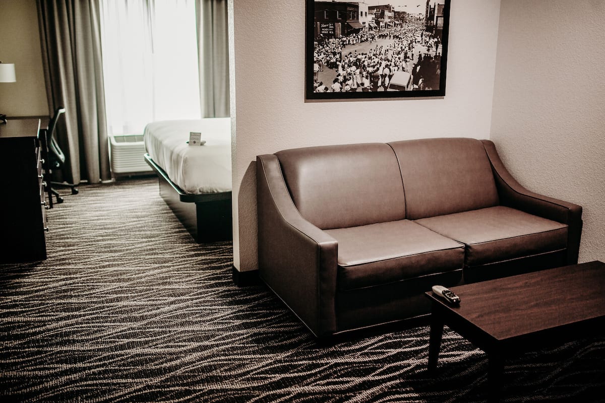 A hotel room with a leather sofa, a small table, a bed, and a wall-mounted picture.