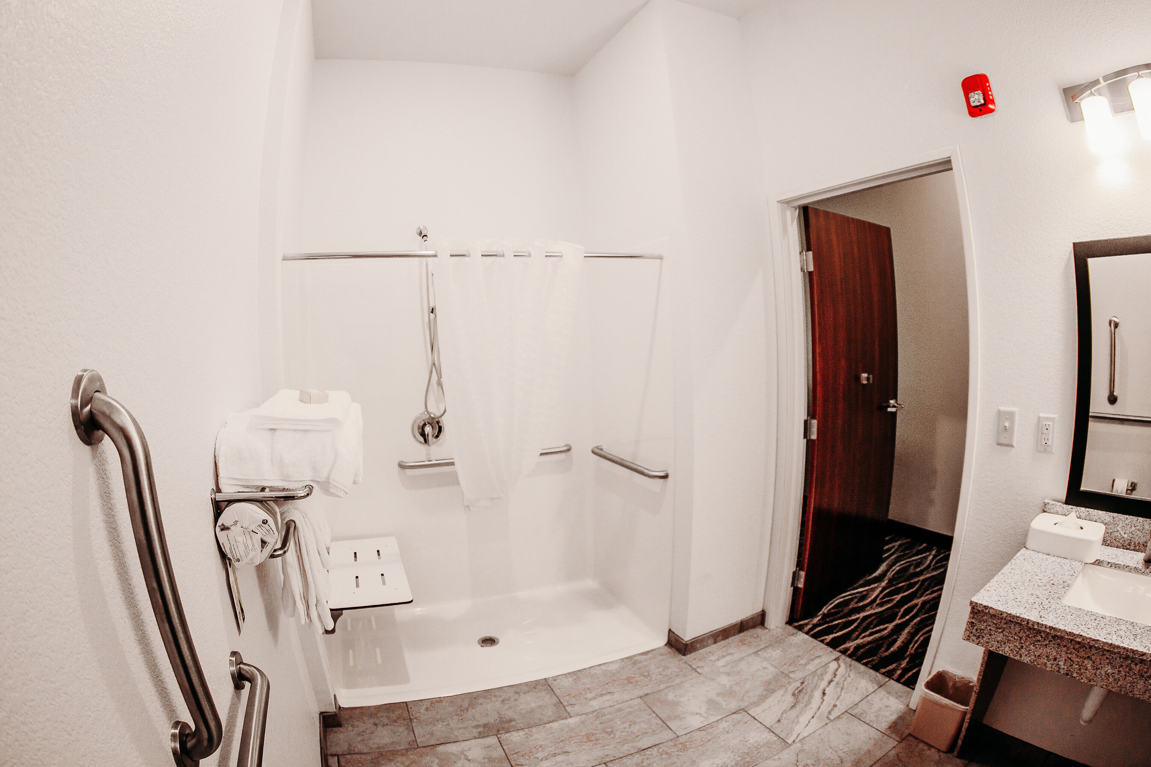 A modern bathroom with a walk-in shower, grab bars, a sink, and a mirror.