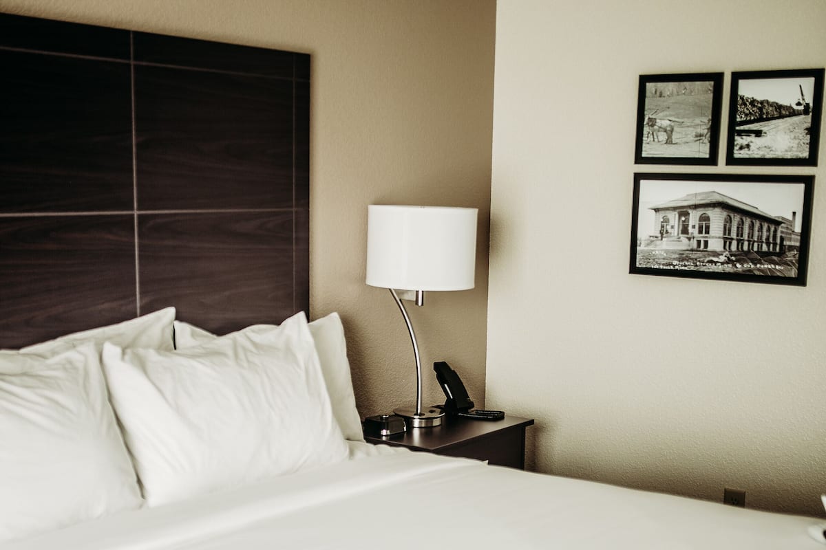 A hotel room with a large bed, a bedside table with a lamp, and three framed pictures on the wall.
