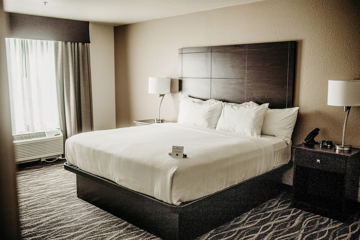 A hotel room with a large bed, two bedside lamps, a nightstand, and a window with curtains.