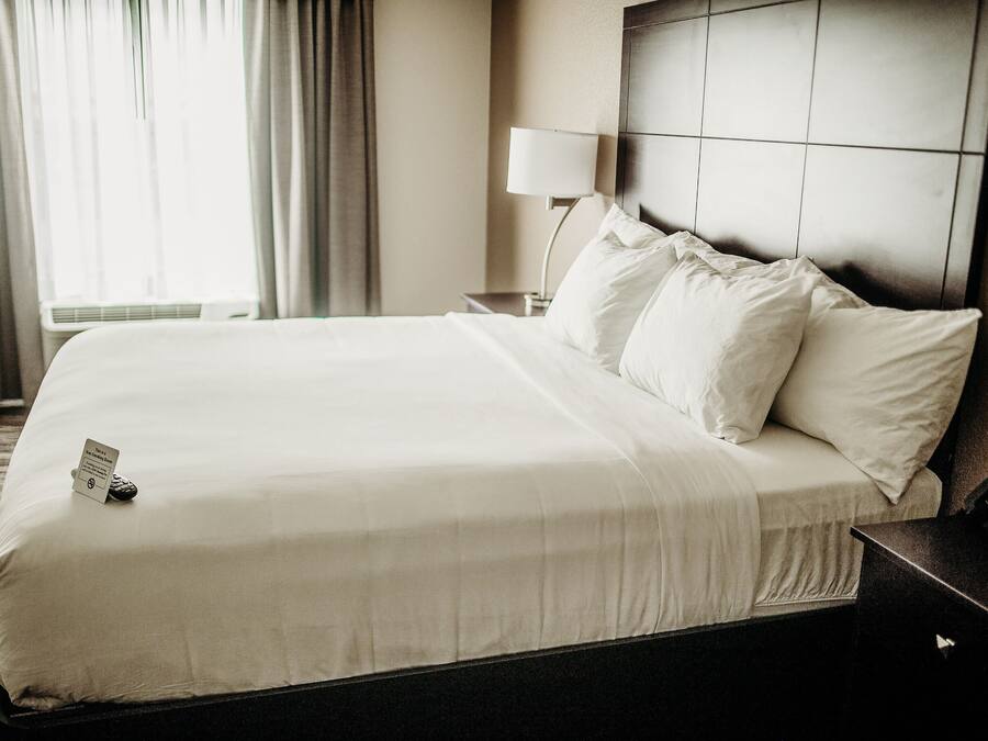 Una cama bien tendida con sábanas blancas, una lámpara de noche y un control remoto sobre la cama.