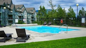 A swimming pool with lounge chairs, a lifeguard tower, and a fenced area with a view of mountains. - 2-Bedroom 2-Bathroom Condo with Mountain Views (Radium Hotsprings)