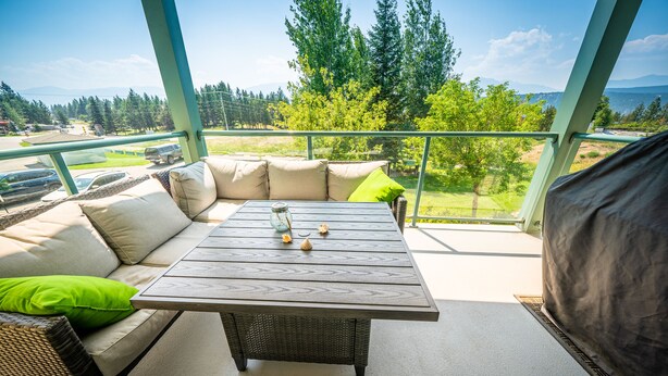 A balcony with a sofa, a table, and a view of a green landscape. - 2-Bedroom 2-Bathroom Condo with Mountain Views (Radium Hotsprings)
