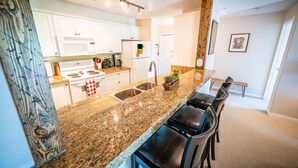 A modern kitchen with white cabinets, a granite countertop, a built-in stove, and a stainless steel sink. - 2-Bedroom 2-Bathroom Condo with Mountain Views (Radium Hotsprings)